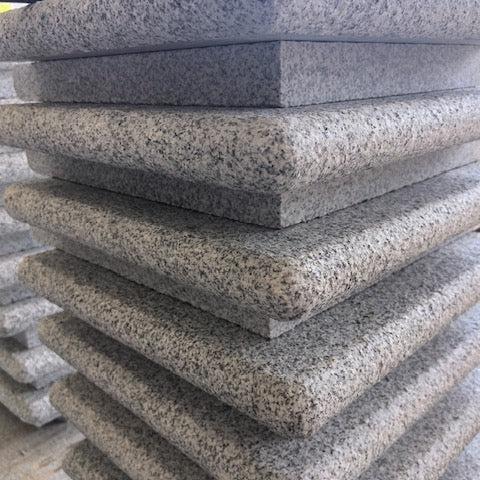 A stack of gray granite bullnose step corners with a flammed top and bullnosed edges.